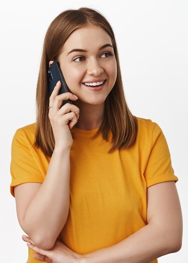 Cellular and technology concept. Young woman talking on mobile phone and smiling, wearing yellow t-shirt. Girl speaking with friend and looking aside, using smartphone, white background.
